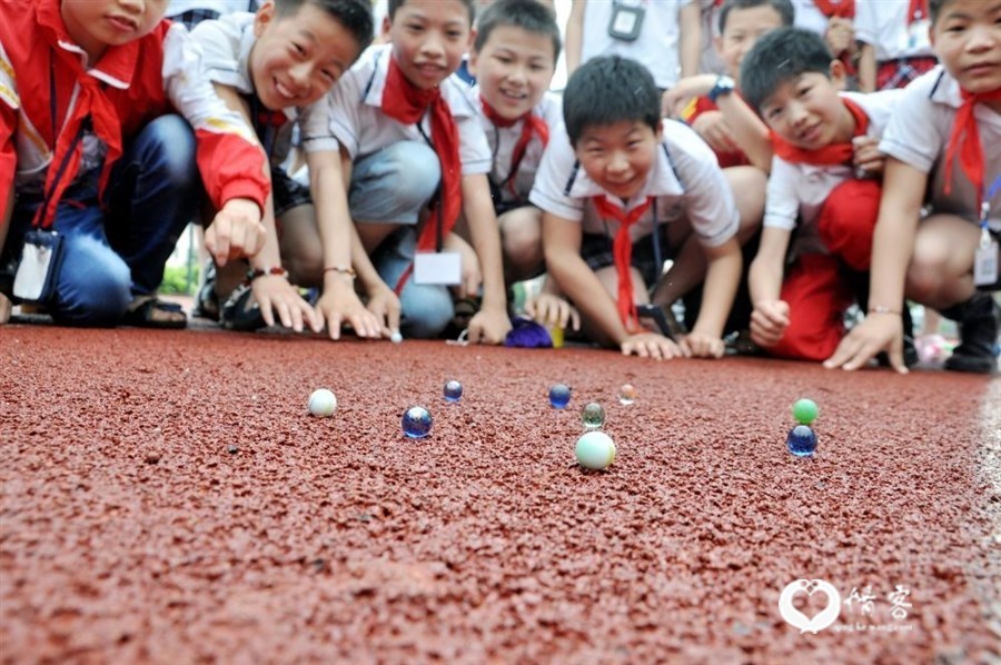 2015年5月27日，在江西省万载县第一小学，孩子们在“寻找父母儿时的老游戏”迎“六一”活动中玩打弹珠。